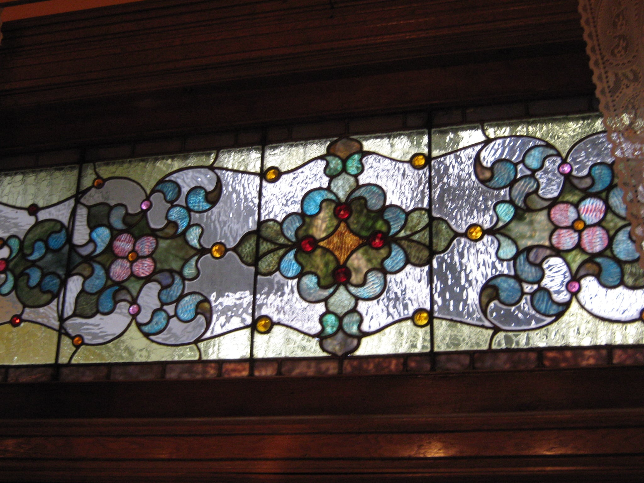 Colorful floral Povey Brothers stained glass panel above wood trim in Deepwood’s parlor
