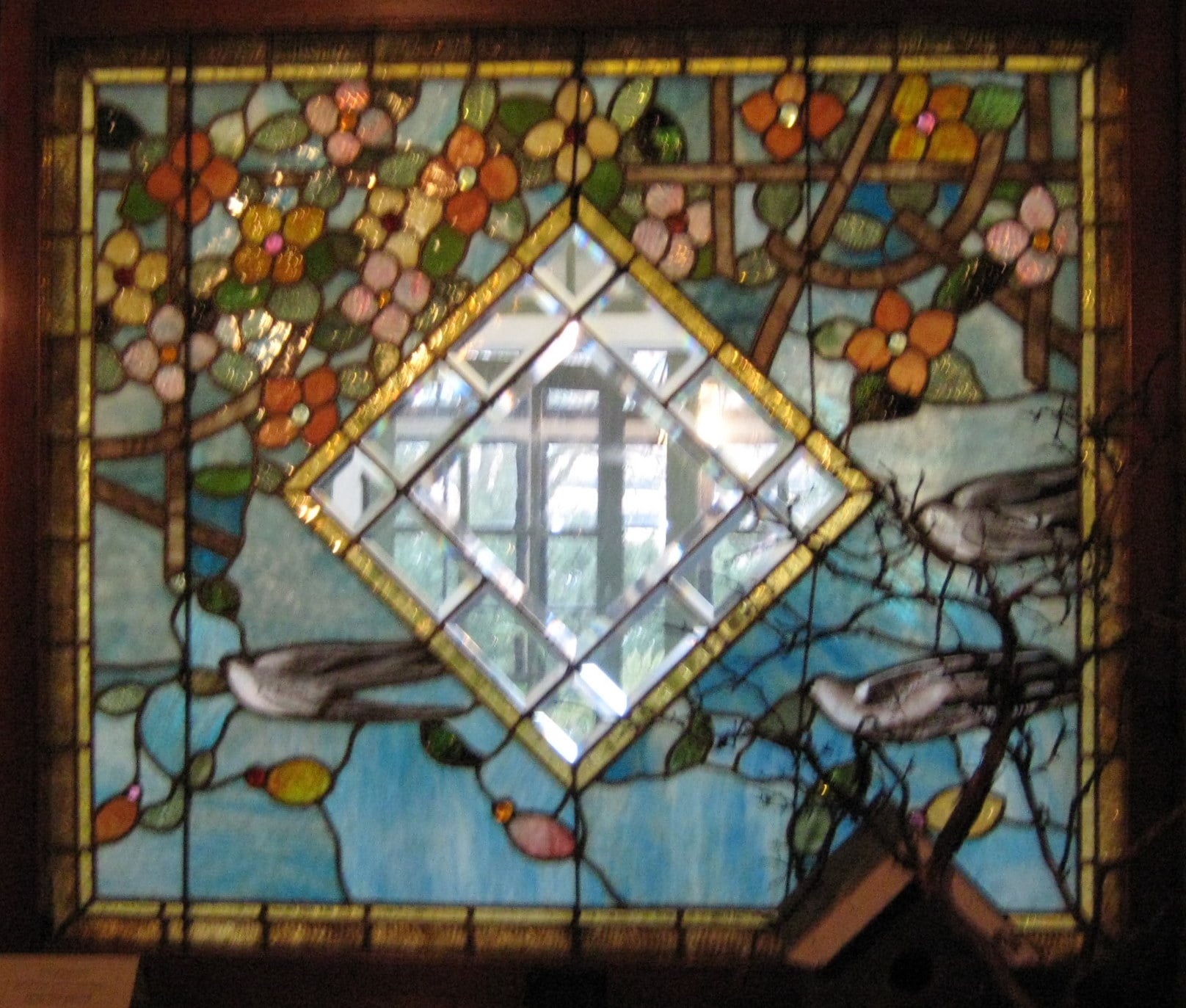 Birds and foliage surrounding a diamond shaped clear pane in stained glass