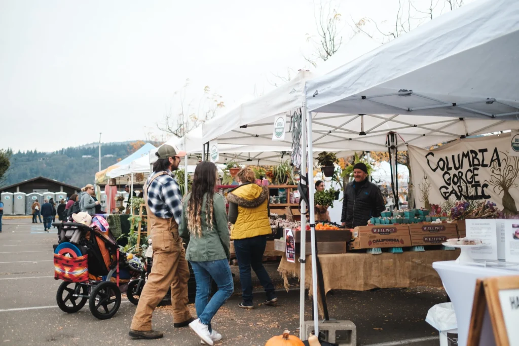 Visitors walking beside white vendor tents and the Columbia Gorge Garlic booth at Hood River Valley Harvest Festival