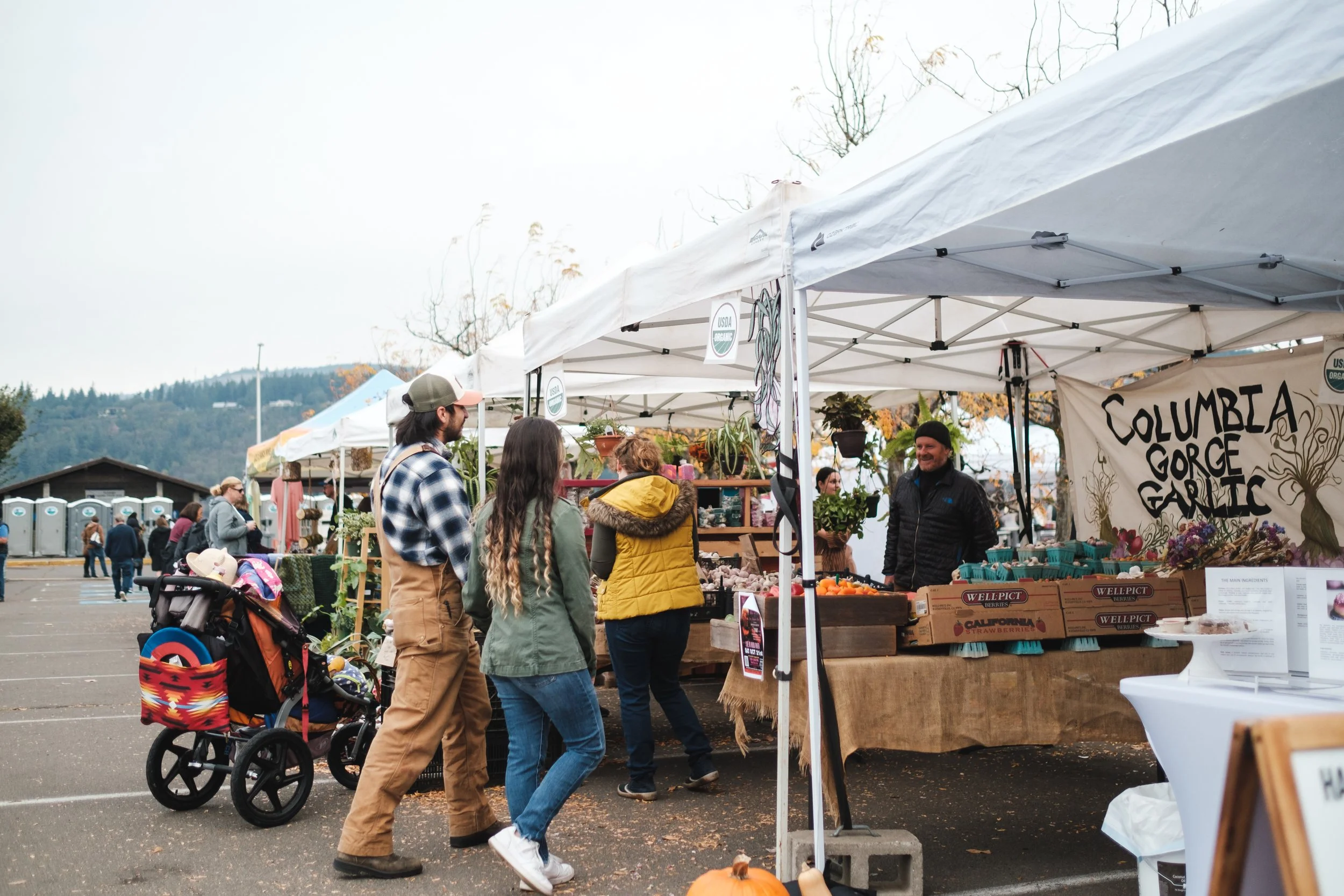 Visitors at Hood River Valley Harvest Festival Visitors walking beside white vendor tents and the Columbia Gorge Garlic booth at Hood River Valley Harvest Festival