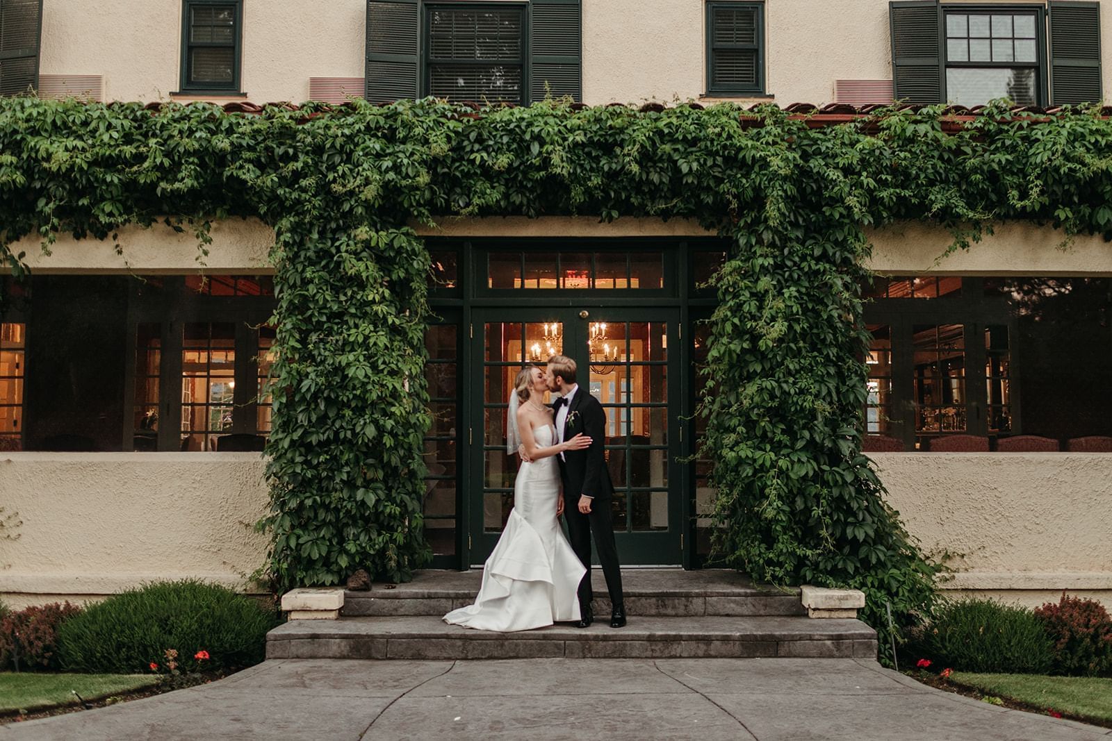 A wedding couple stands at the ivy-framed Columbia Gorge Hotel entrance.