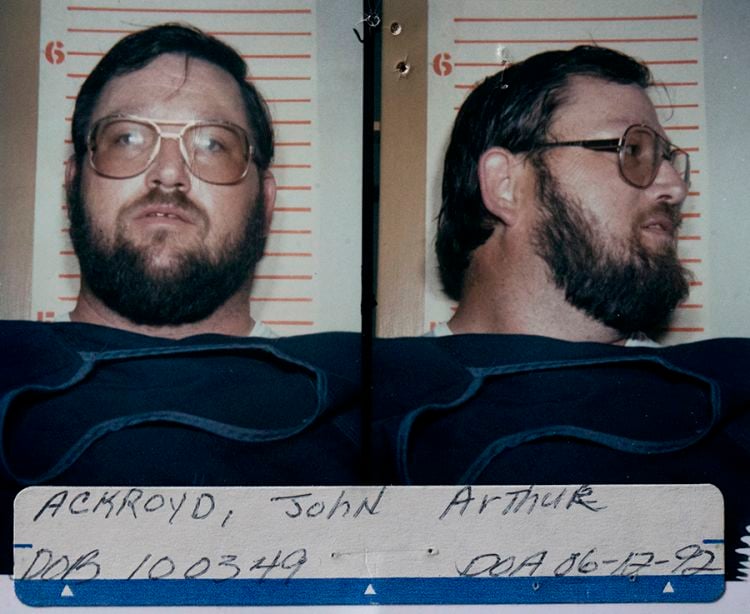 Front and profile booking photographs of John Arthur Ackroyd in 1992, wearing glasses and a dark shirt in front of a height chart.