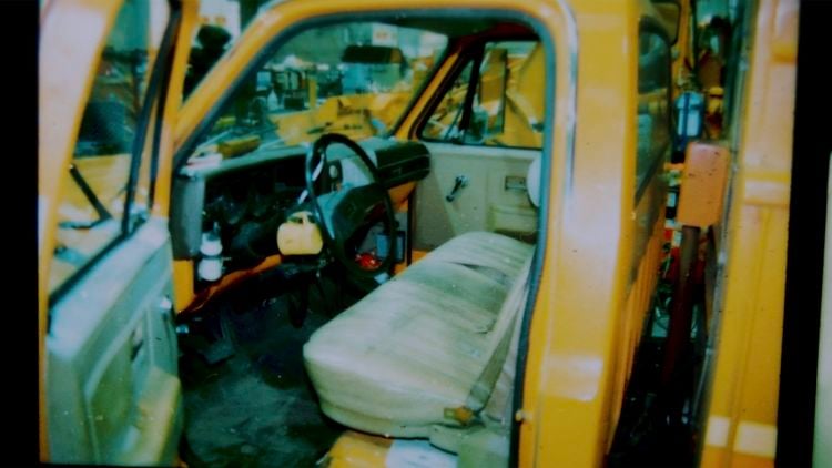 Archival photograph looking through an open door into a yellow work truck, showing the steering wheel and bench seat.