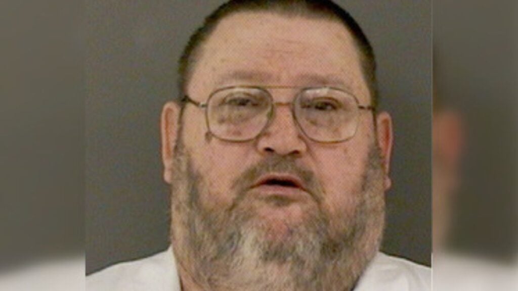 Oregon Department of Corrections portrait of John Arthur Ackroyd wearing glasses, with a gray beard.