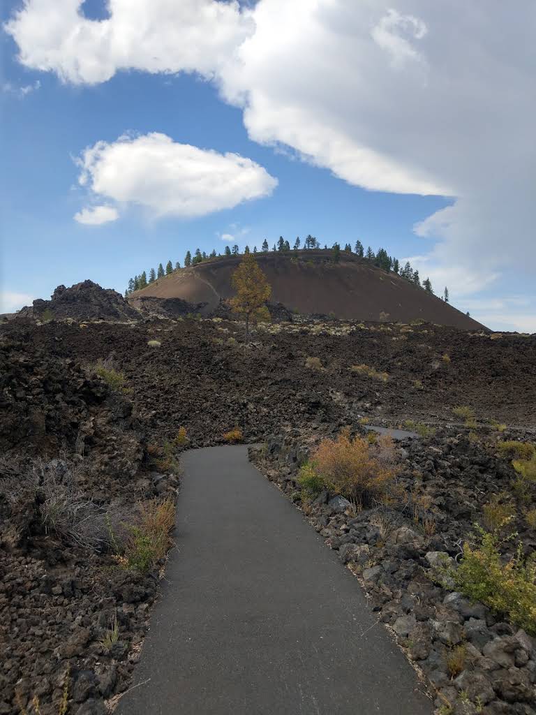 Paved trail through dark lava with Lava Butte rising beyond it