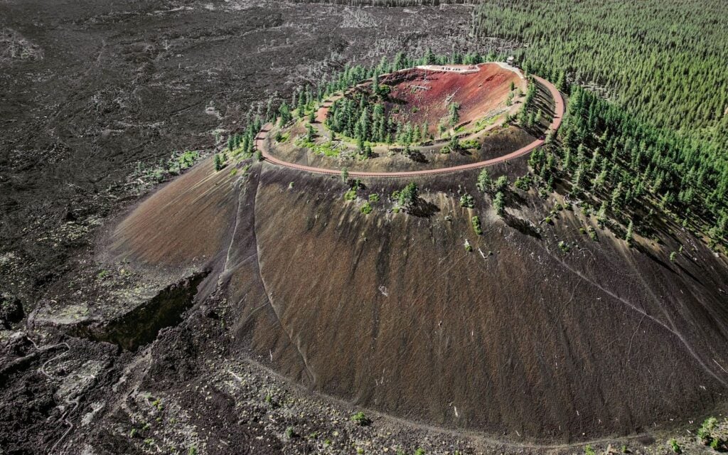 Aerial view of Lava Butte’s red crater and summit road surrounded by forest and dark lava fields