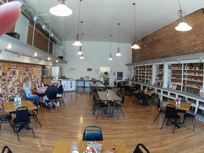 The café dining room with exposed brick walls, a high ceiling, hanging lights, wood floors, and tables
