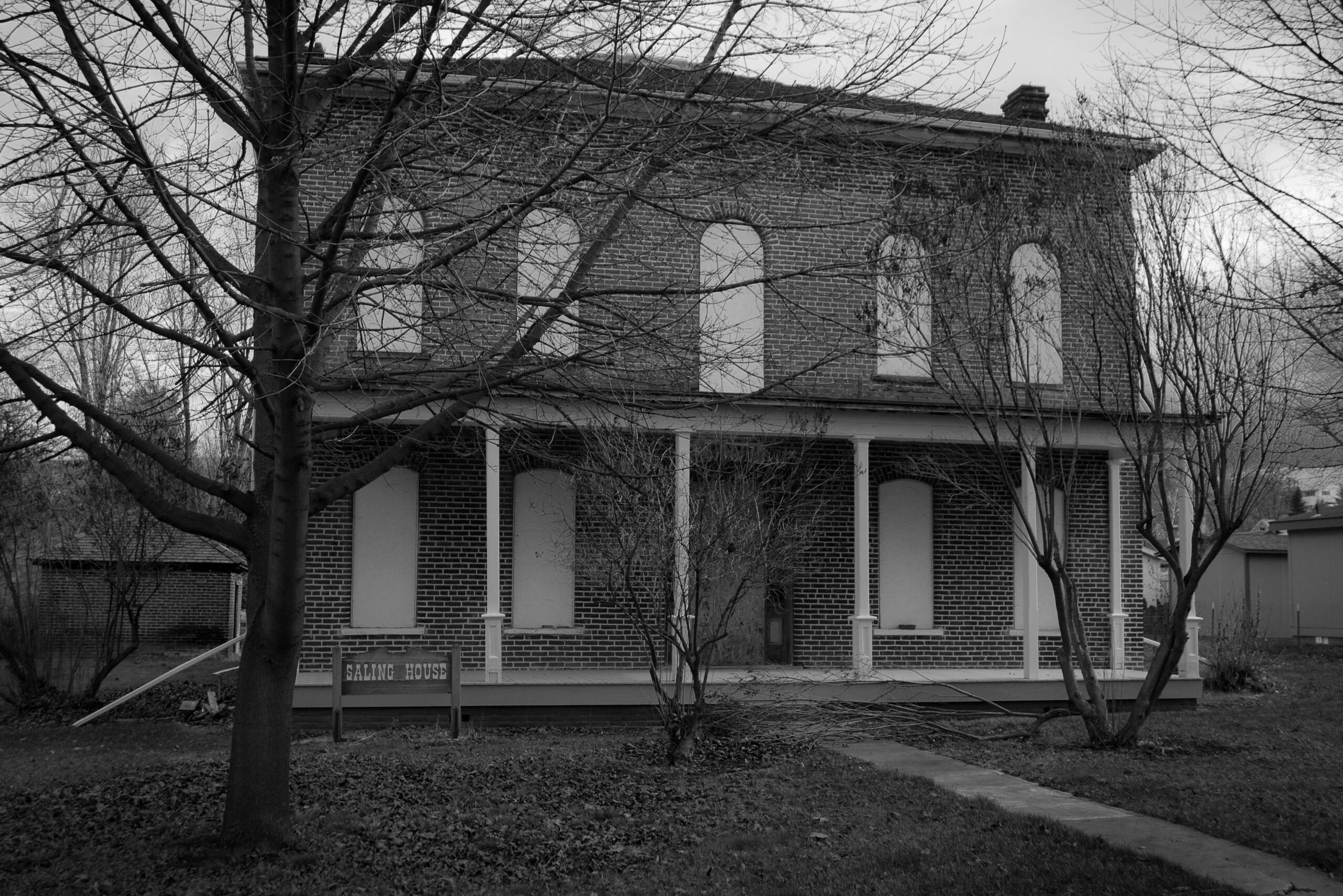 A black and white photograph of Weston's two story brick Isham Saling House behind bare trees