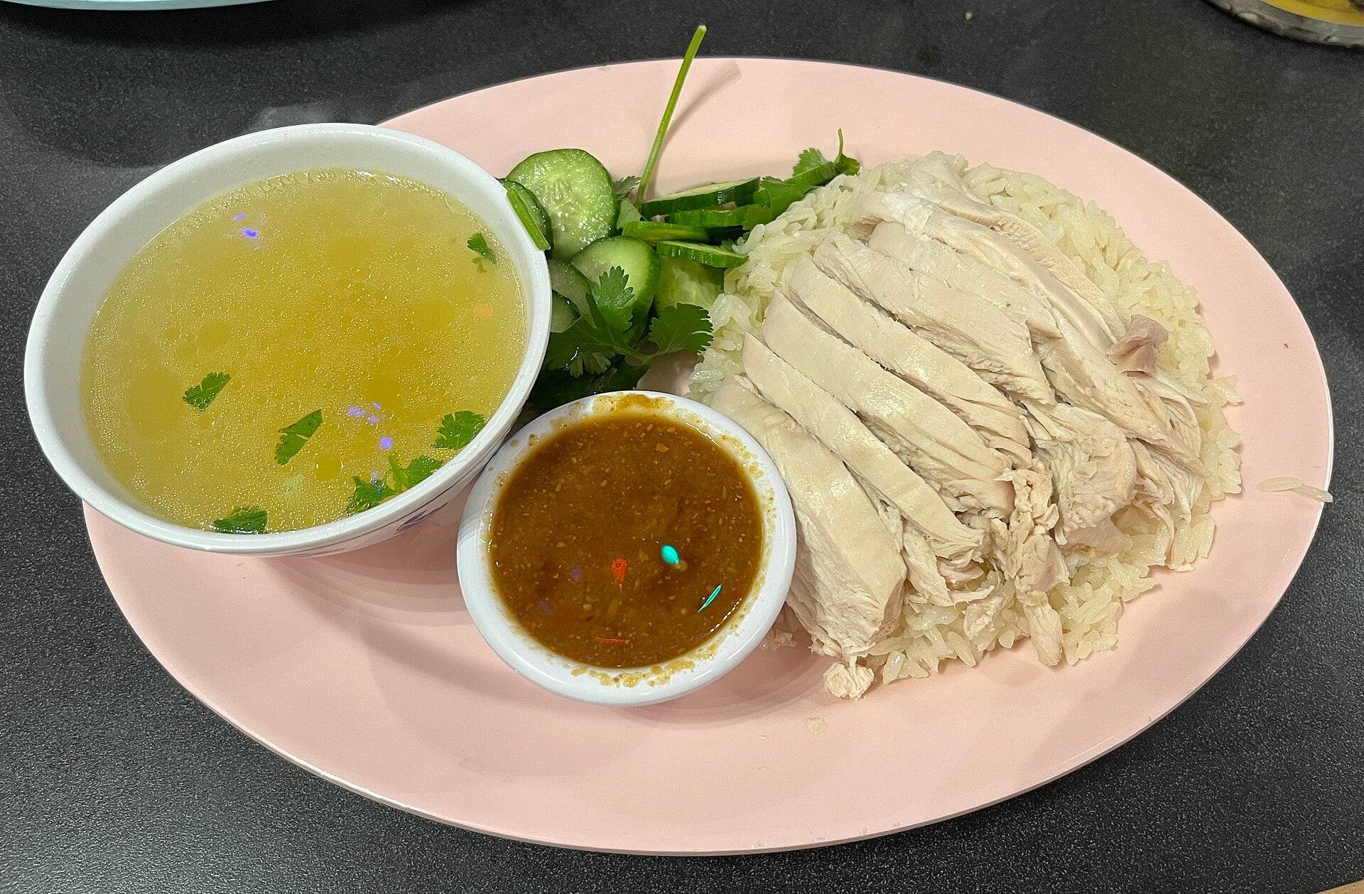 Sliced chicken over rice with cucumber, cilantro, sauce and soup at Nong’s