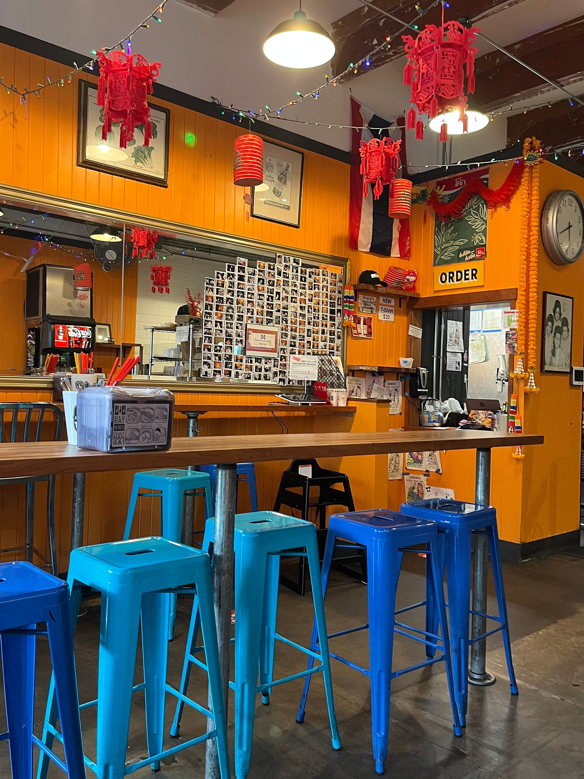 Blue stools and wooden tables beneath red lanterns in the orange dining room at Nong’s