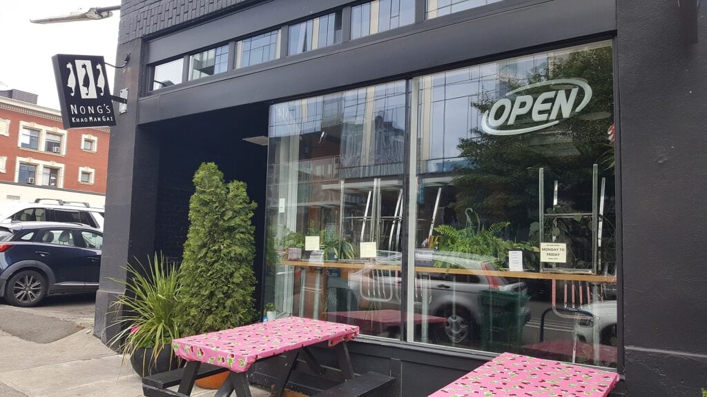Black Nong’s Khao Man Gai storefront with large windows and pink floral picnic tables