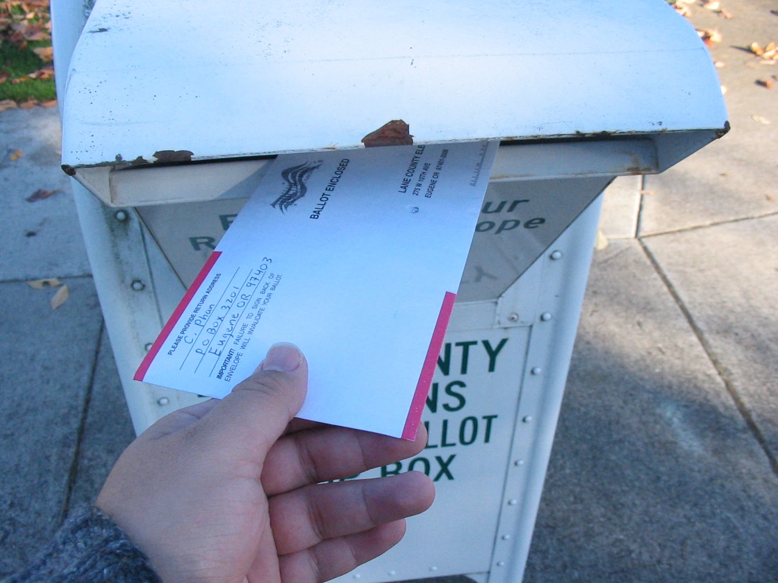 Oregon voter returning ballot in Lane County in 2006 A hand places a completed ballot envelope into a Lane County Oregon drop box in 2006