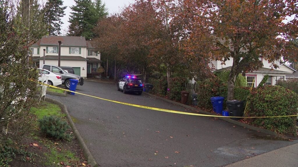 Police tape crosses a driveway outside an Oregon City home, with a police vehicle parked nearby.