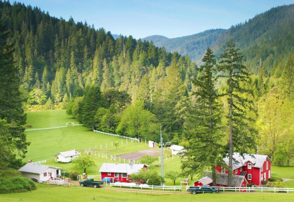 Ranch buildings and open lawn surrounded by steep forested hills in the Rogue River canyon