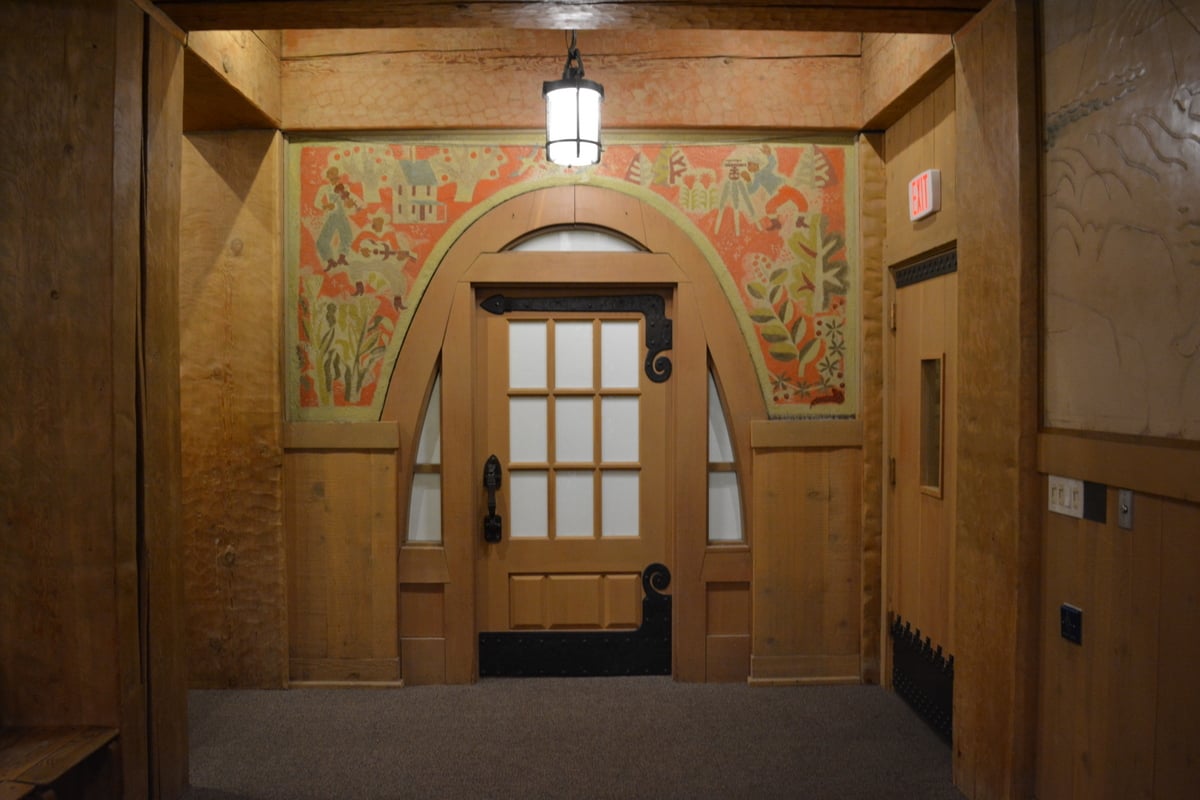 Wooden door with decorative ironwork beneath a colorful painted mural at Timberline Lodge