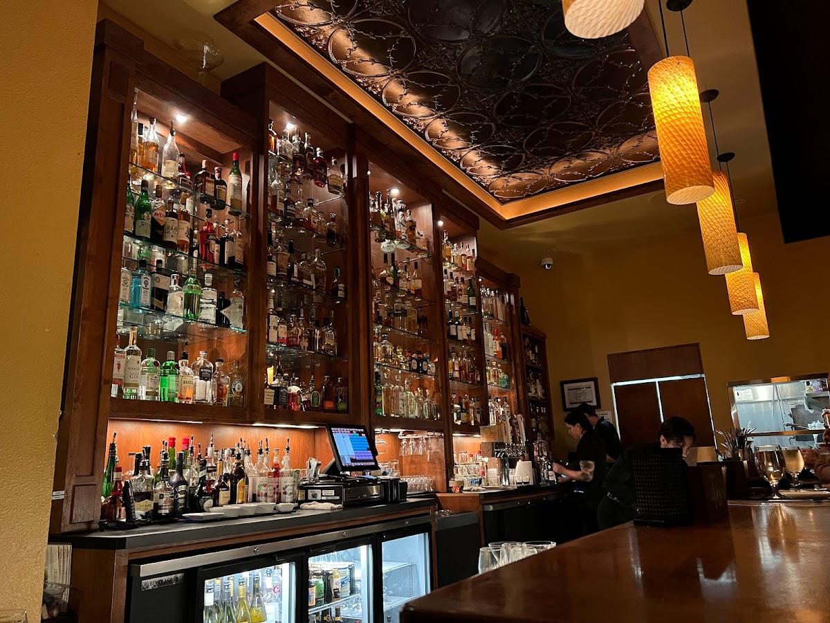 Bottles on tall shelves behind the bar at Vault 244, with pendant lights and a patterned tin ceiling overhead.