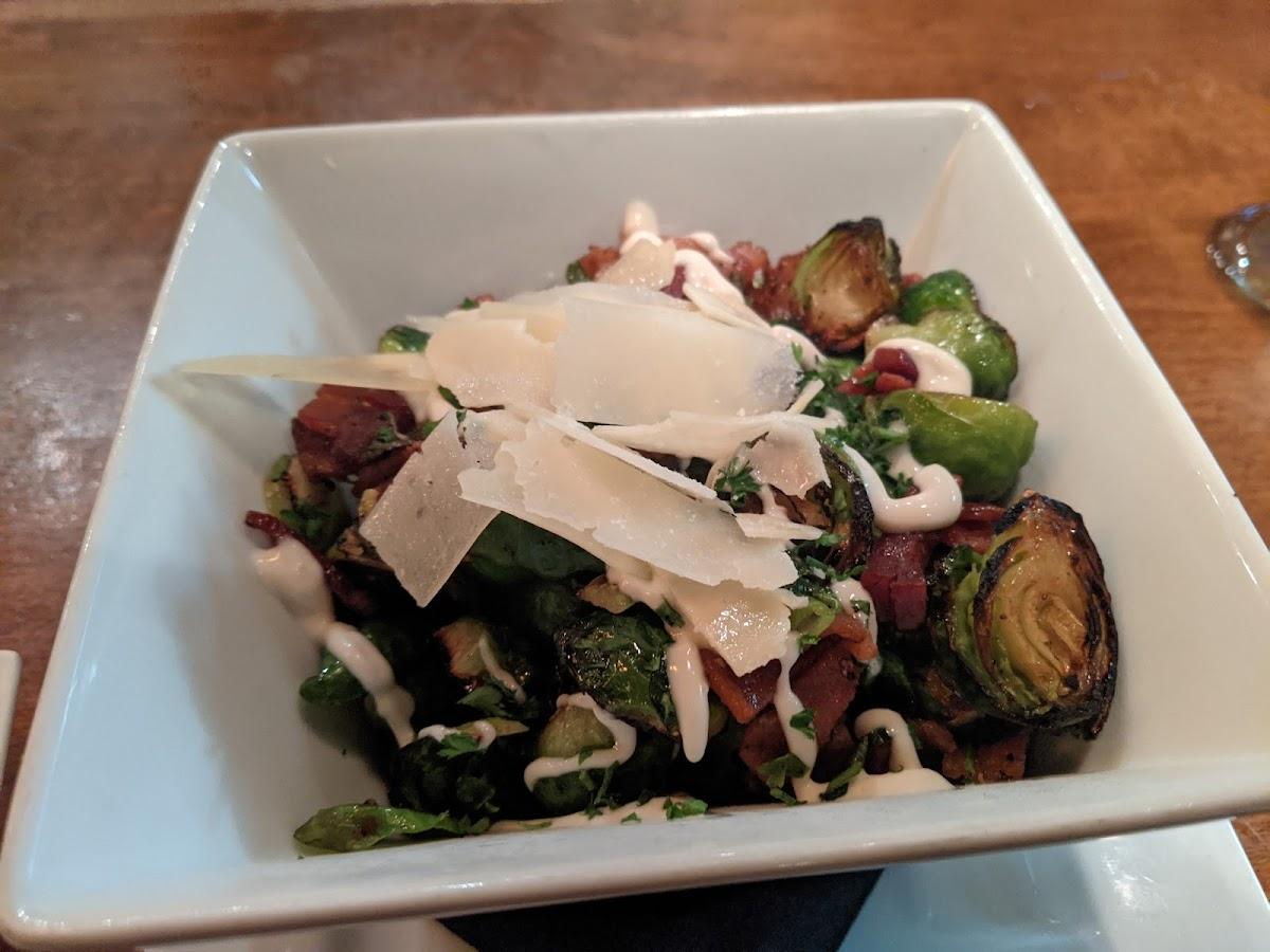 Brussels sprouts topped with bacon, sauce, and shaved cheese in a white bowl at Vault 244.